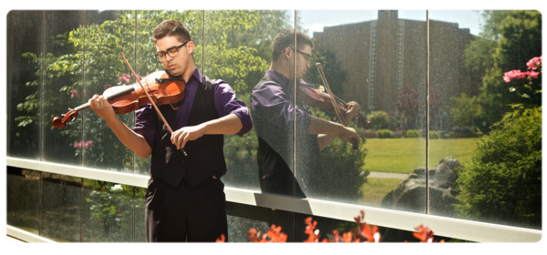 音乐 major plays violin outside - flowers in the foreground, surface reflecting the university church in the background